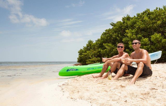 Two young guys relax on a beach and enjoy a glass of wine while taking a break from their kayaking tour in Key West