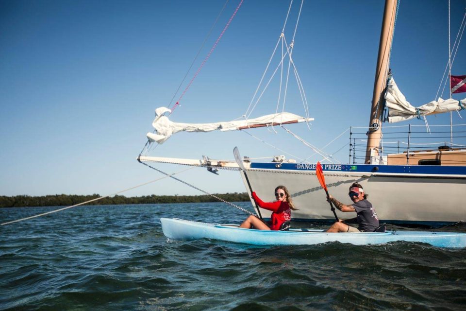A couple paddle a blue kayak next to a schooner in the waters near Key West