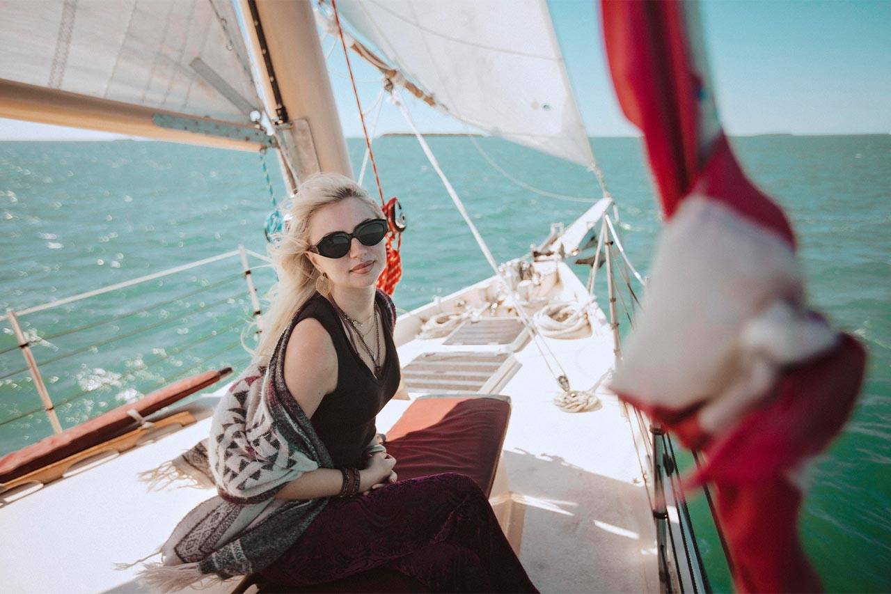 A blond woman wearing a dark dress and sunglasses relaxes while sailing on a schooner in Key West