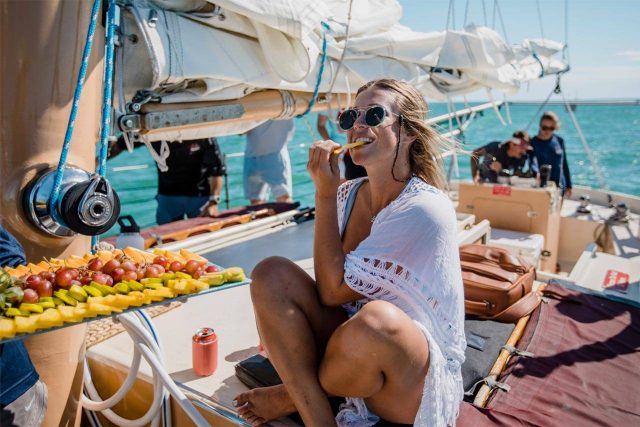 A woman in a white coverup enjoys a piece of fruit aboard a sailing charter in Key West