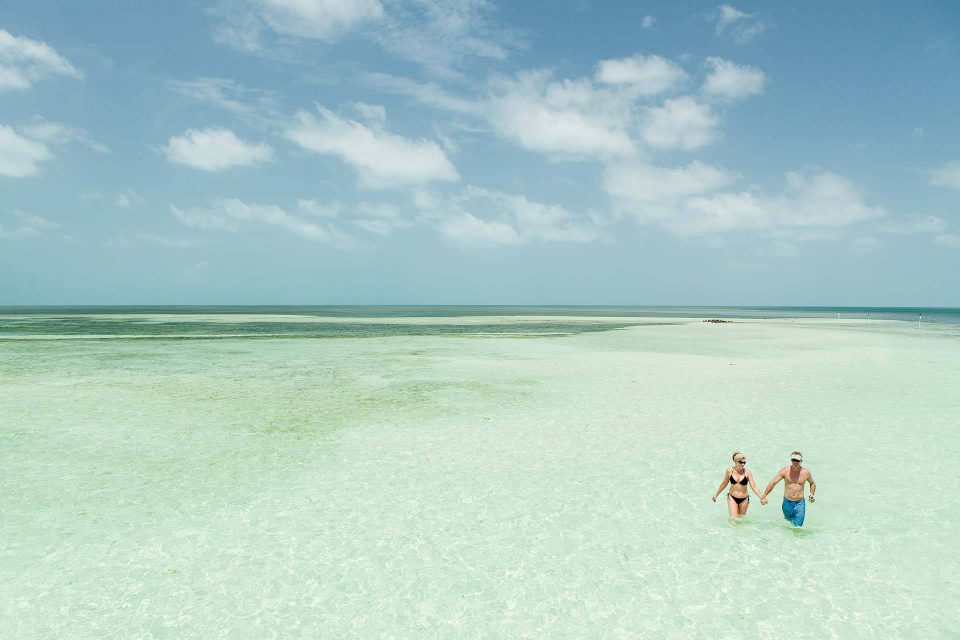 A couple walks in clear blue waters while holding hands in Key West