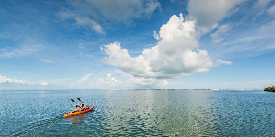 Two women in an orange kayak paddle in calm waters near Key West, FL