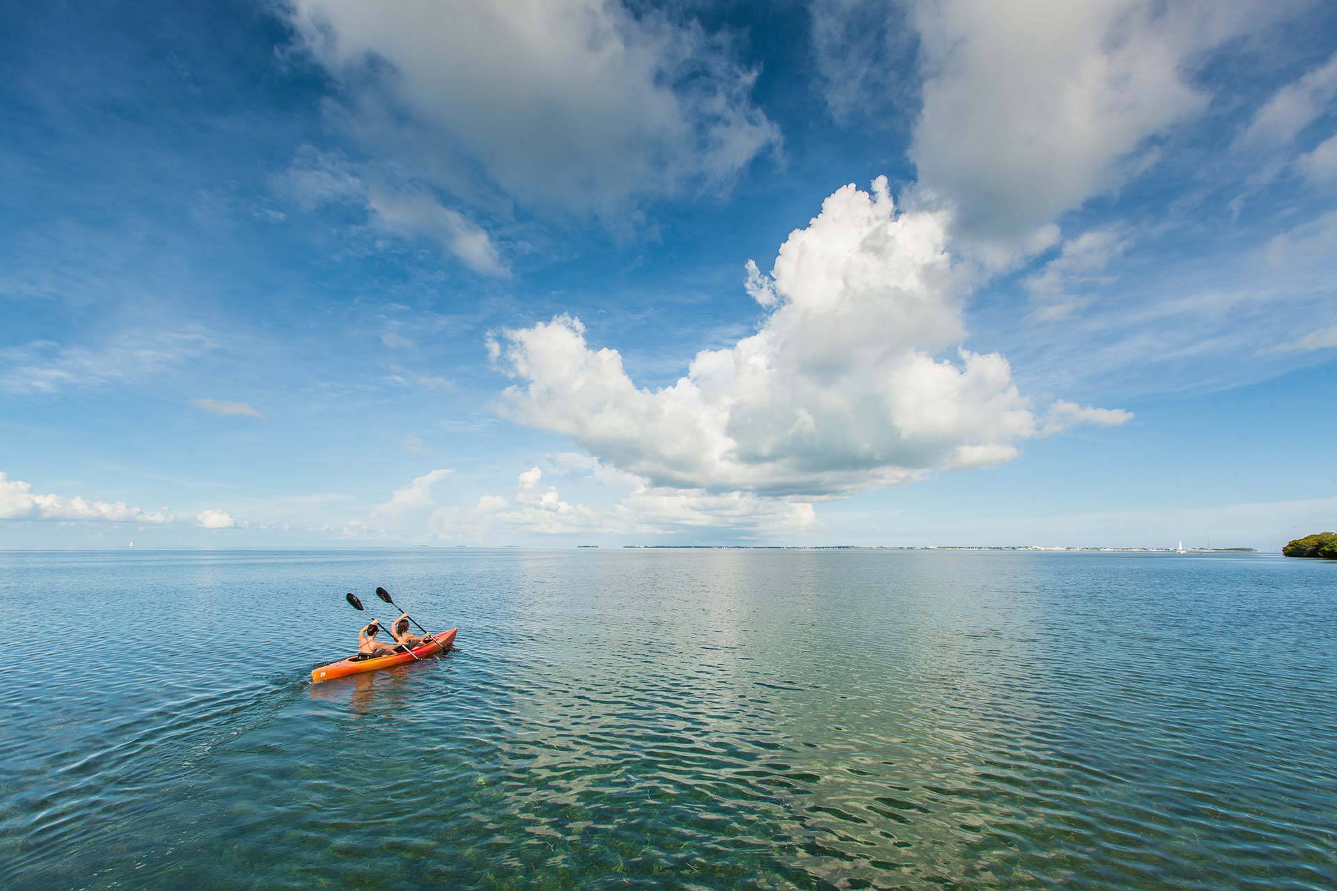 Two women in an orange kayak paddle in calm waters near Key West, FL