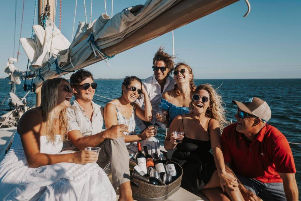 A group of young friends relax and drink wine while on a sailing charter with Danger Charters in Key West, FL